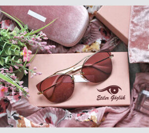 Stylish sunglasses with gold frames and pink-tinted lenses placed on a custom-printed sunglasses box, branded